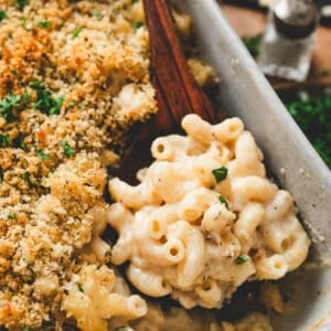 A wooden spoon lifting a scoop of Guinness mac and cheese from a baking dish.
