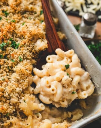 A wooden spoon lifting a scoop of Guinness mac and cheese from a baking dish.