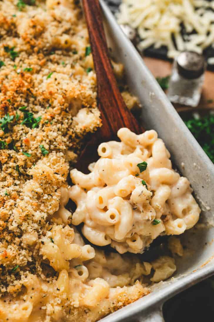 A wooden spoon lifting a scoop of Guinness mac and cheese from a baking dish.
