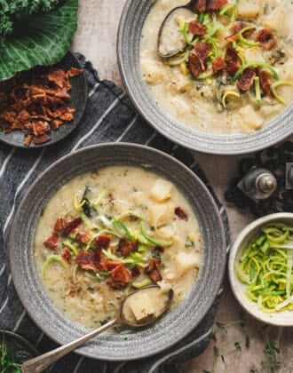 Two gray bowls filled with a cabbage potato soup recipe and topped with bacon and sliced leeks.