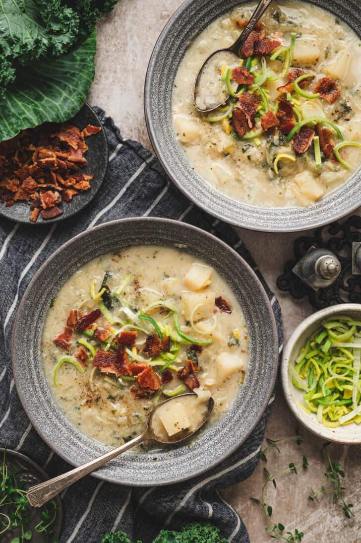 Two gray bowls filled with a cabbage potato soup recipe and topped with bacon and sliced leeks.