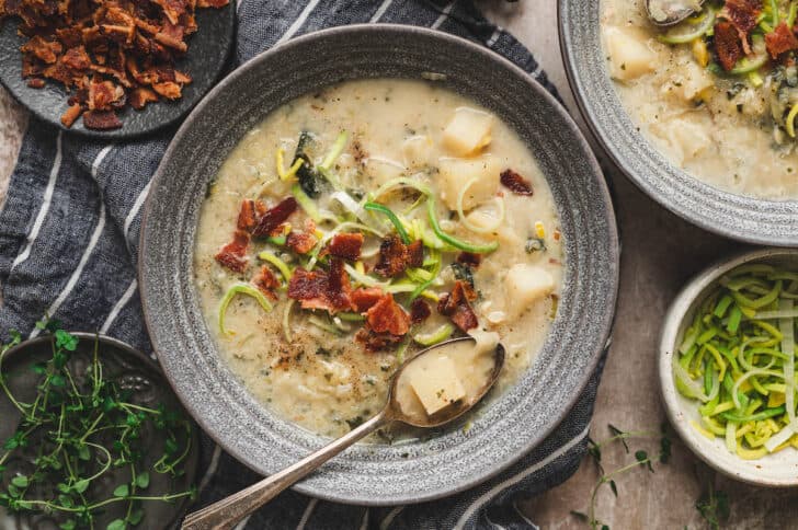A gray bowl filled with an Irish bacon cabbage and potato soup and topped with bacon and sliced leeks.
