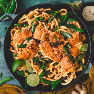 Curry udon noodles topped with salmon and snap peas in a large skillet.