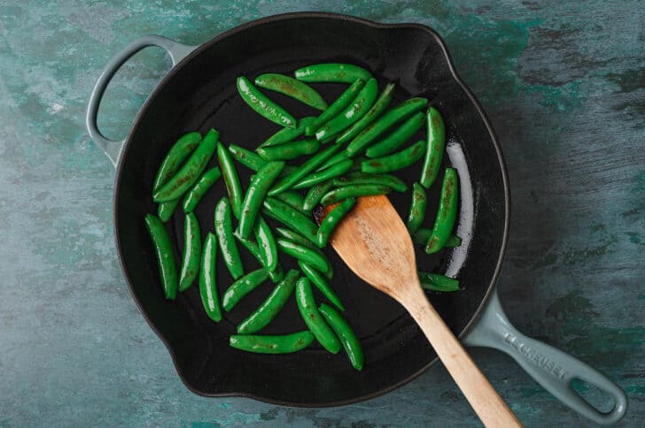 Snap peas being sauteed in a large skillet.