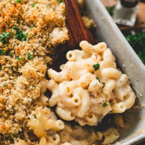 A wooden spoon lifting a scoop of Guinness mac and cheese from a baking dish.
