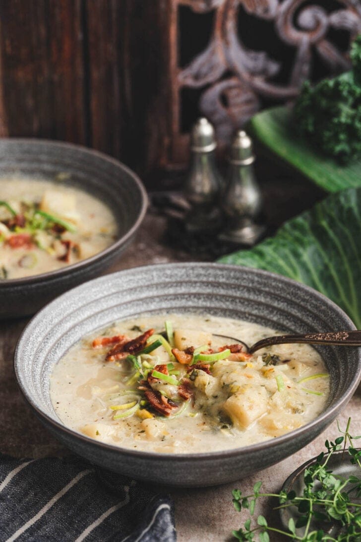 Two gray bowls filled with an Irish potato cabbage soup and topped with bacon and sliced leeks.