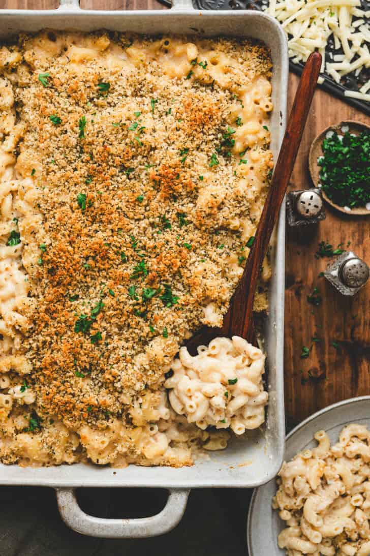 A wooden spoon lifting a scoop of a Guinness mac and cheese recipe from a baking dish.