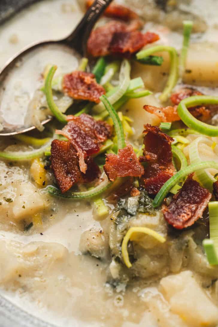 Closeup on Irish cabbage soup topped with bacon and sliced leeks.