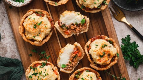 A cutting board filled with mini shepherd's pies.
