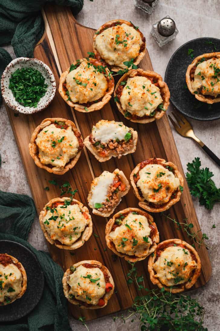 A cutting board filled with mini shepherd's pies.