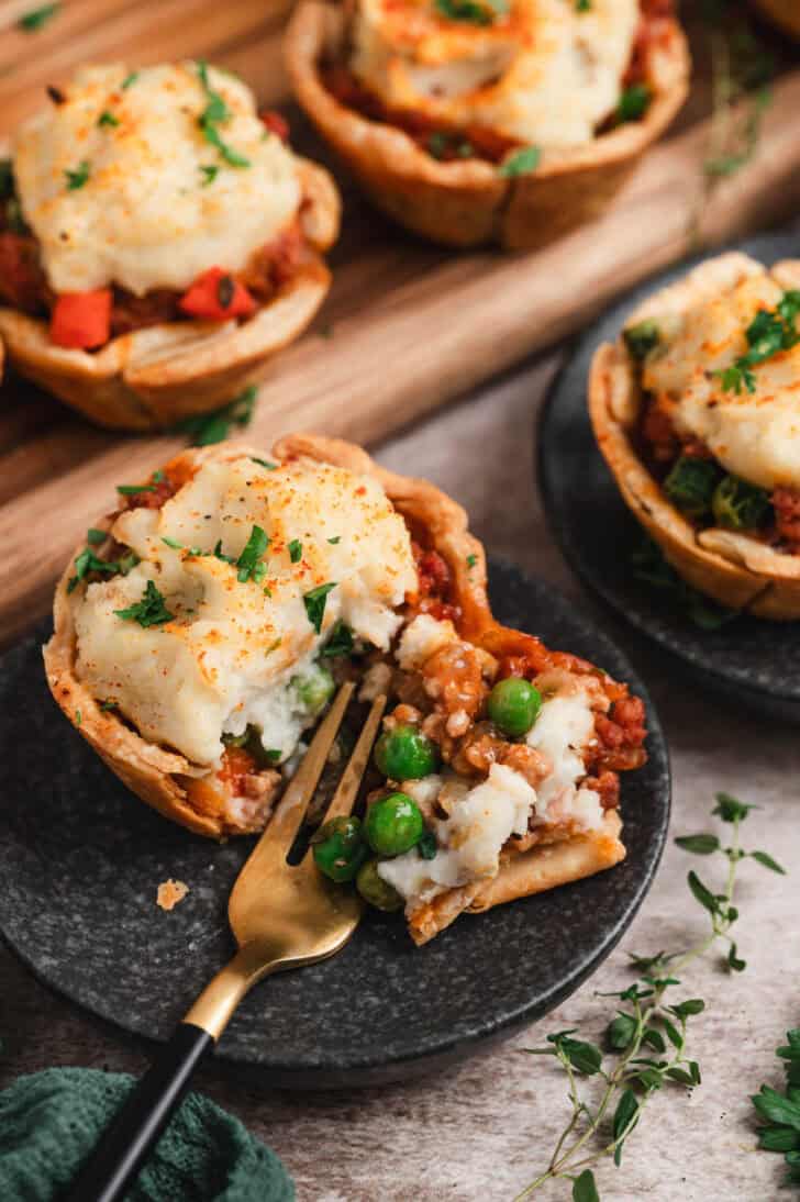 An individual shepherd's pie on a small dark plate, with a fork breaking into it.