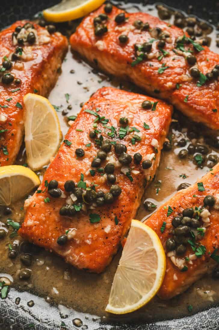 Several pieces of salmon piccata in a skillet.