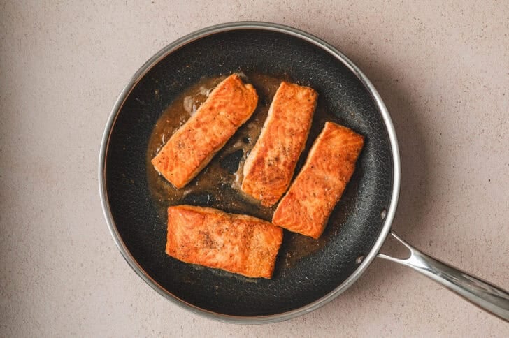 Four pieces of salmon being seared in a skillet.