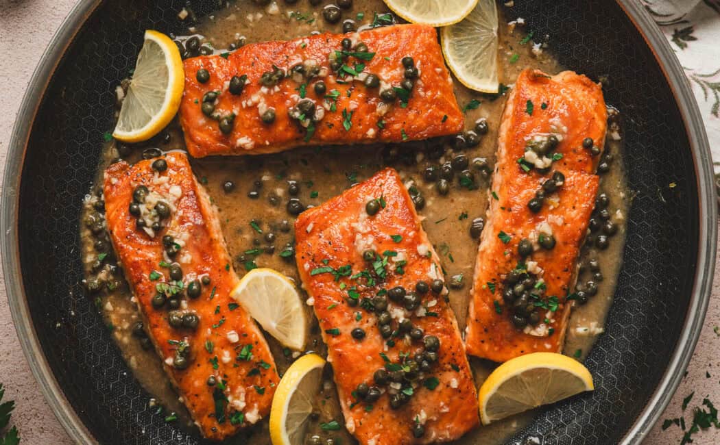 A skillet filled with four pieces of salmon piccata.