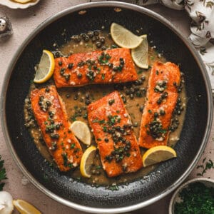 A skillet filled with four pieces of salmon piccata.
