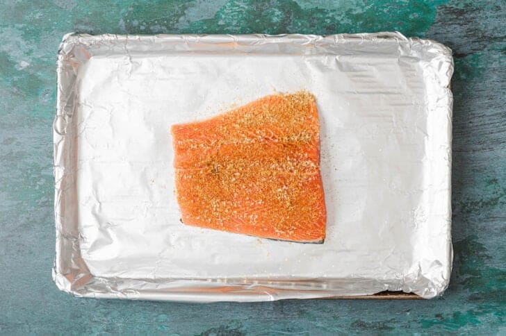 A piece of raw pink fish seasoned with spices on a baking pan.