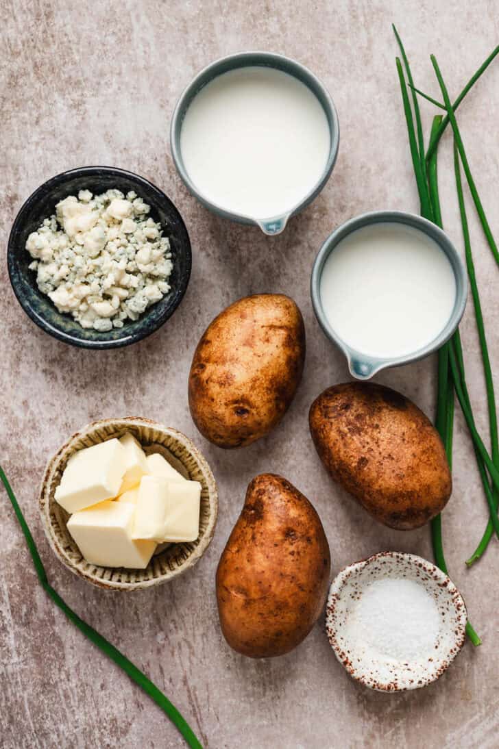 Ingredients on a gray background, including potatoes, dairy ingredients, blue cheese, salt and chives.