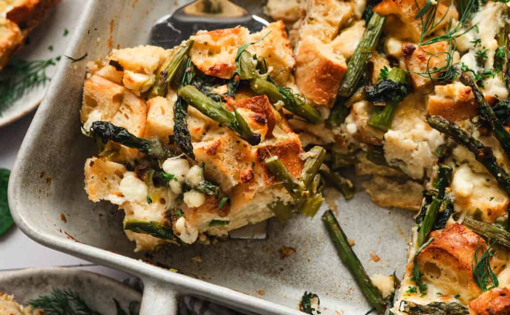 A server lifting a piece of strata recipe from a baking dish.