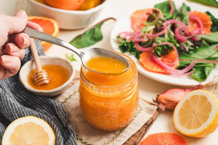 A spoon lifting some salad dressing for citrus salad from a glass jar.