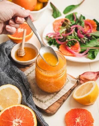 A spoon lifting some citrus vinaigrette from a glass jar with salad fixings in the background and foreground.