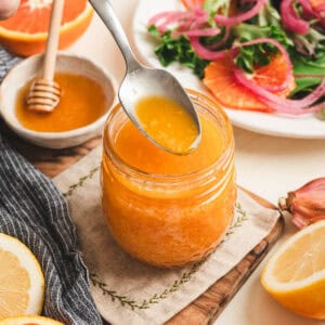 A spoon lifting some citrus vinaigrette from a glass jar with salad fixings in the background and foreground.