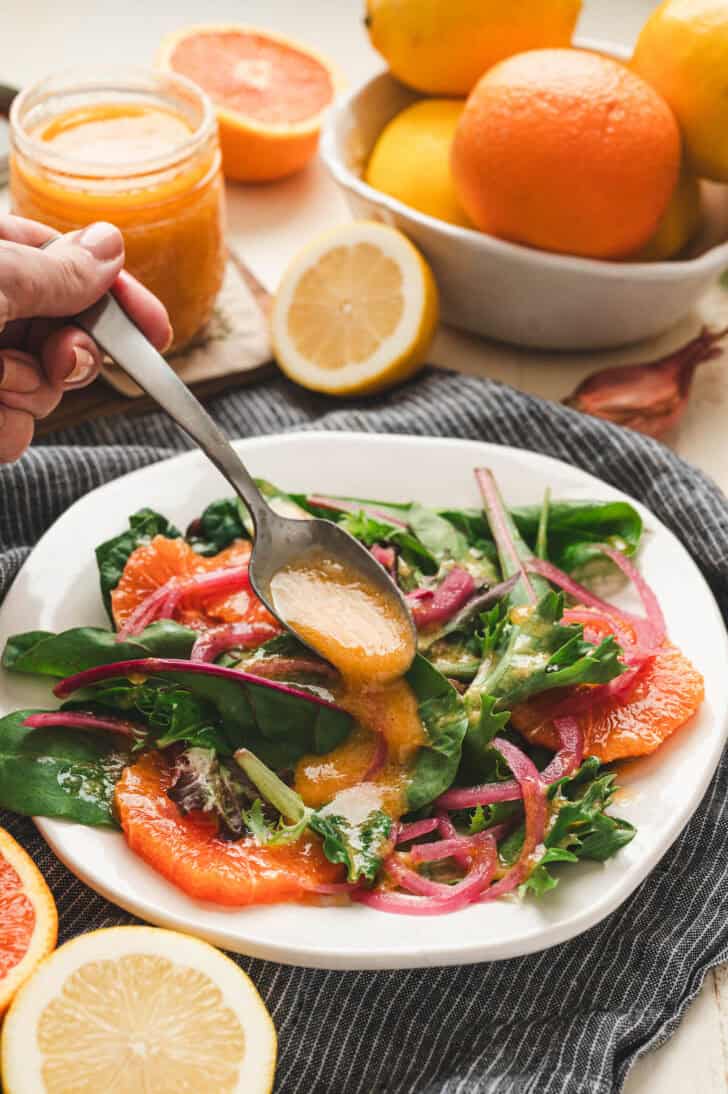 A spoon drizzling citrus dressing over a salad on a white plate.