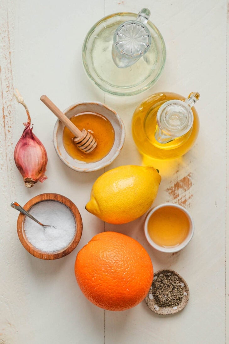 Ingredients on a light surface, including lemon, orange, oils, honey and spices.