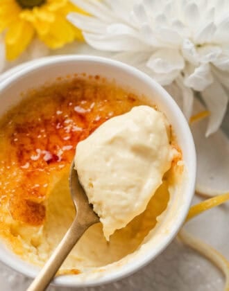 A spoon lifting a bite of lemon creme brulee from a white ramekin.