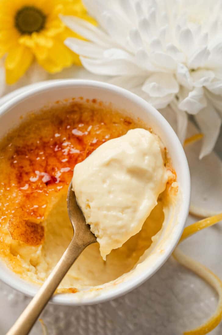 A spoon lifting a bite of lemon creme brulee from a white ramekin.