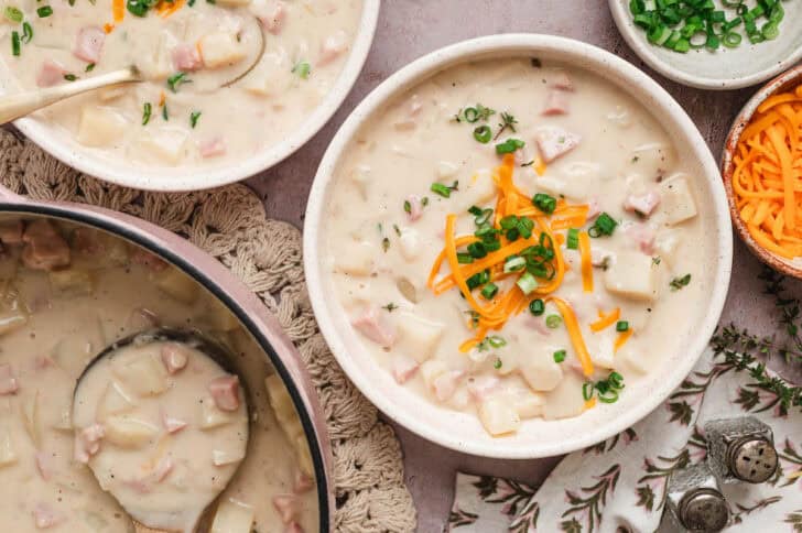 A bowl of ham bone potato soup topped with shredded cheese and green onions.
