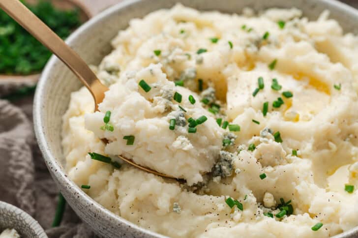 A bowl of blue cheese mashed potatoes with a serving spoon scooping some.