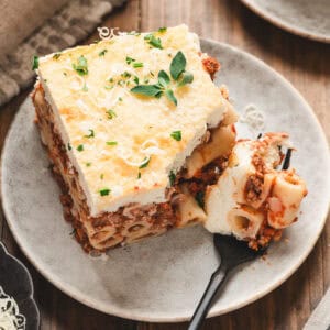 A slice of Greek lasagna on a small plate, with a fork taking a bite off the piece.