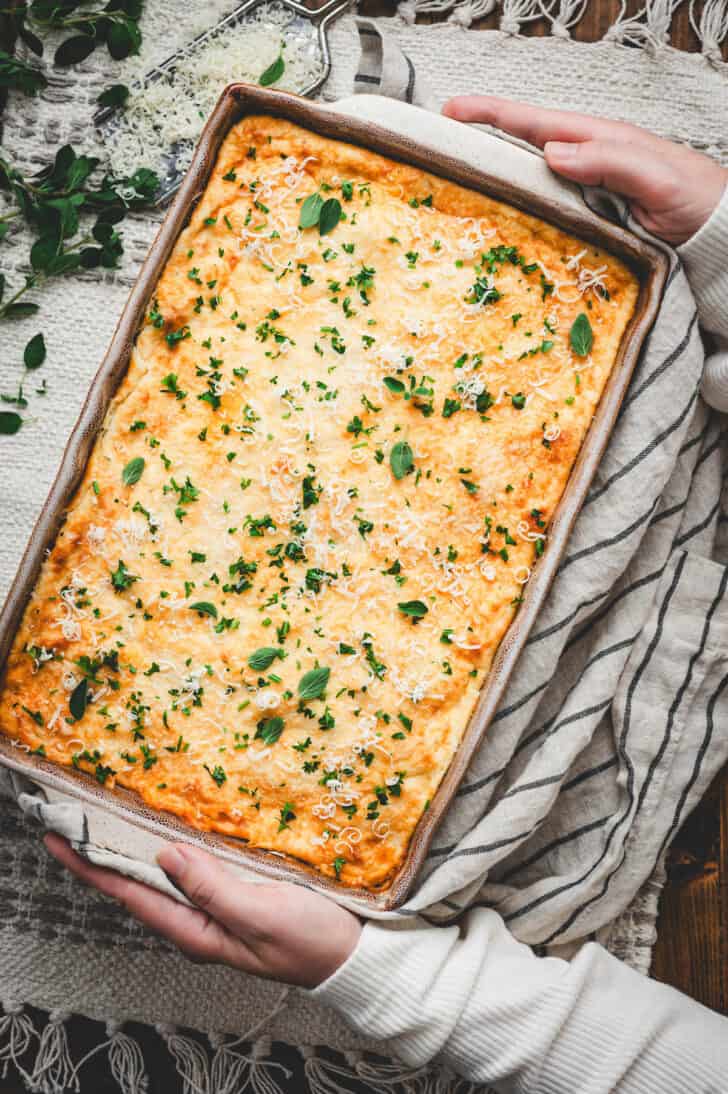 Two hands holding a baking dish filled with Greek lasagna.