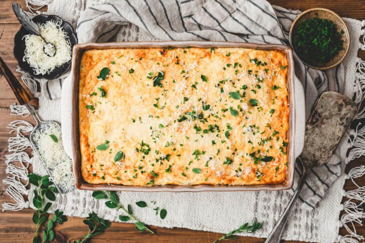 A baking dish filled with Greek pastitsio, sprinkled with herbs.