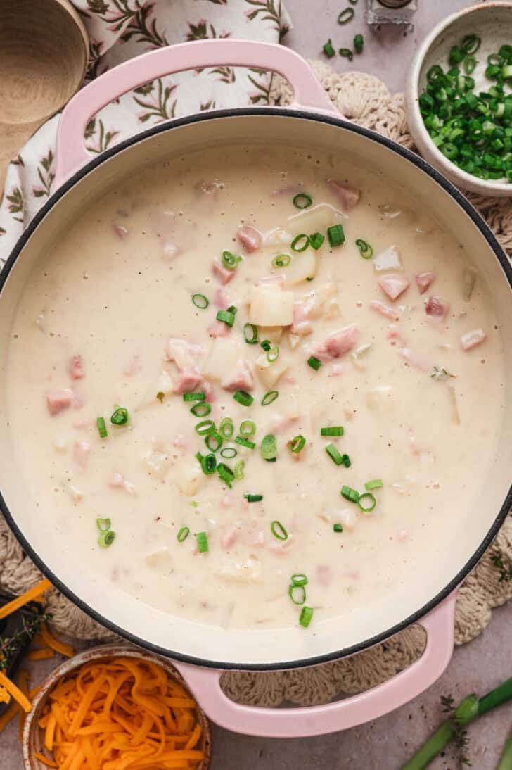 A pink Dutch oven filled with simple ham and potato soup.