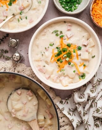 A bowl of potato ham soup alongside the pot with a wooden spoon in it.