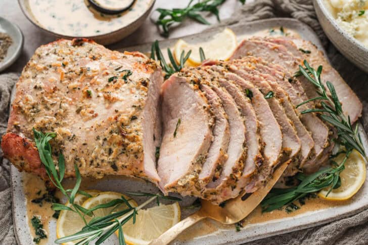 A herb crusted pork loin roast sliced and presented on a serving platter.