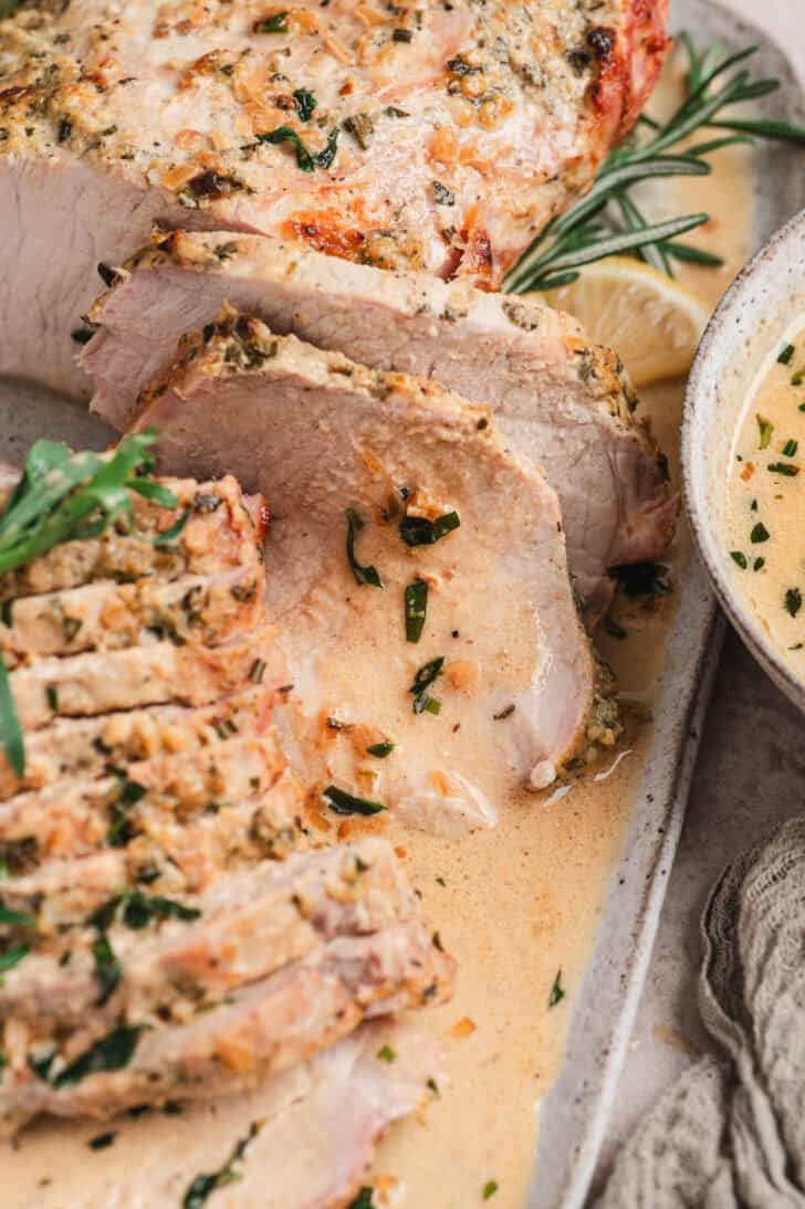 A sliced herb roasted pork roast drizzled with sauce.