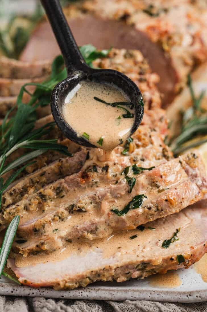 A black spoon drizzling sauce over a pork loin roast recipe.