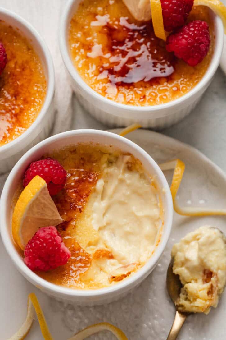 A ramekin of a lemon creme brulee recipe with a spoonful taken out of it and rested to the side on a white plate.