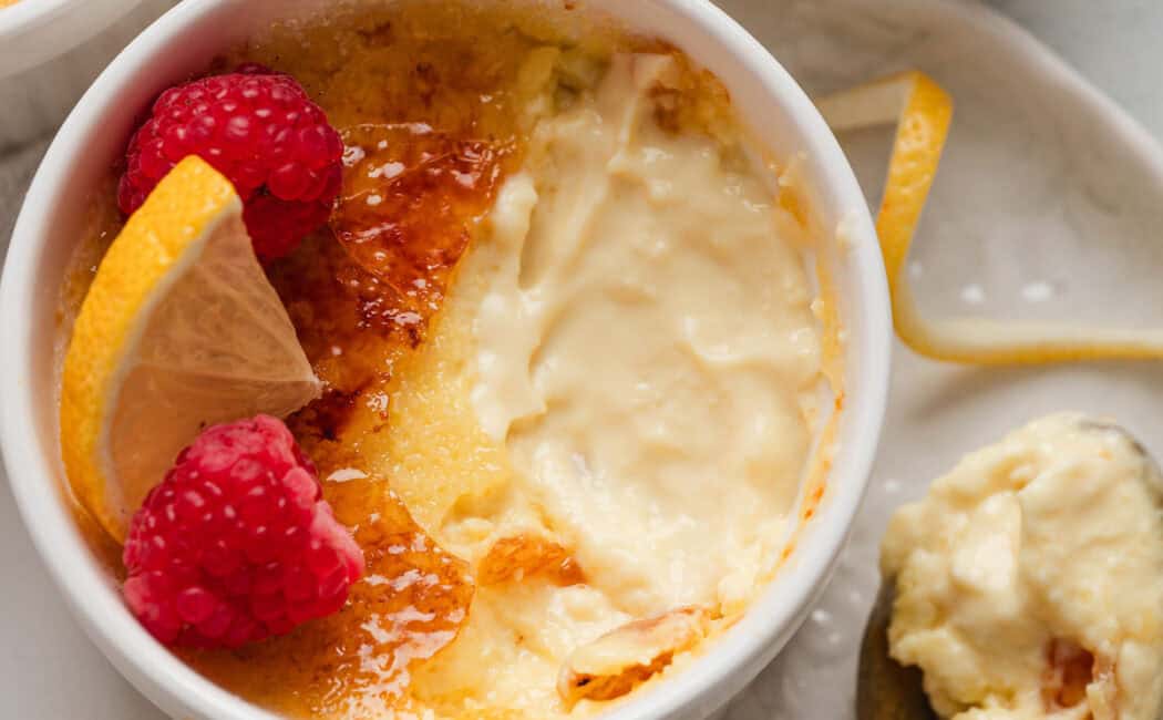 A ramekin of a lemon creme brulee recipe with a spoonful taken out of it and rested to the side on a white plate.