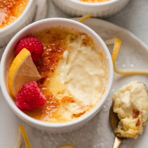 A ramekin of a lemon creme brulee recipe with a spoonful taken out of it and rested to the side on a white plate.