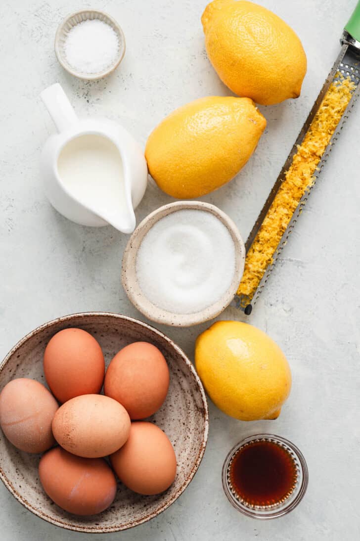 Ingredients on a white surface, including lemons, eggs, vanilla and dairy.