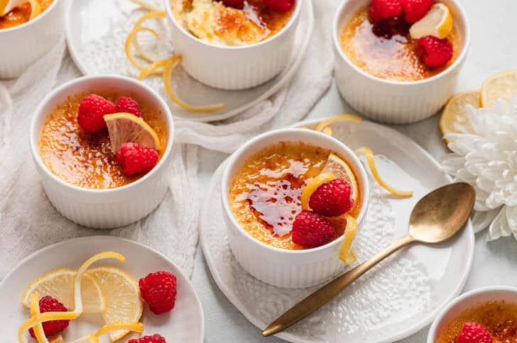 Ramekins of a lemon brulee recipe, garnished with berries and lemon peel.