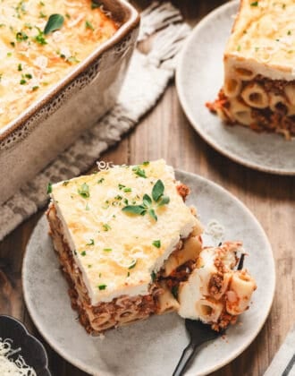 A slice of Greek lasagna on a small plate, with a fork taking a bite off the piece.