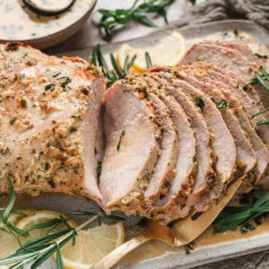 A herb crusted pork loin roast sliced and presented on a serving platter.