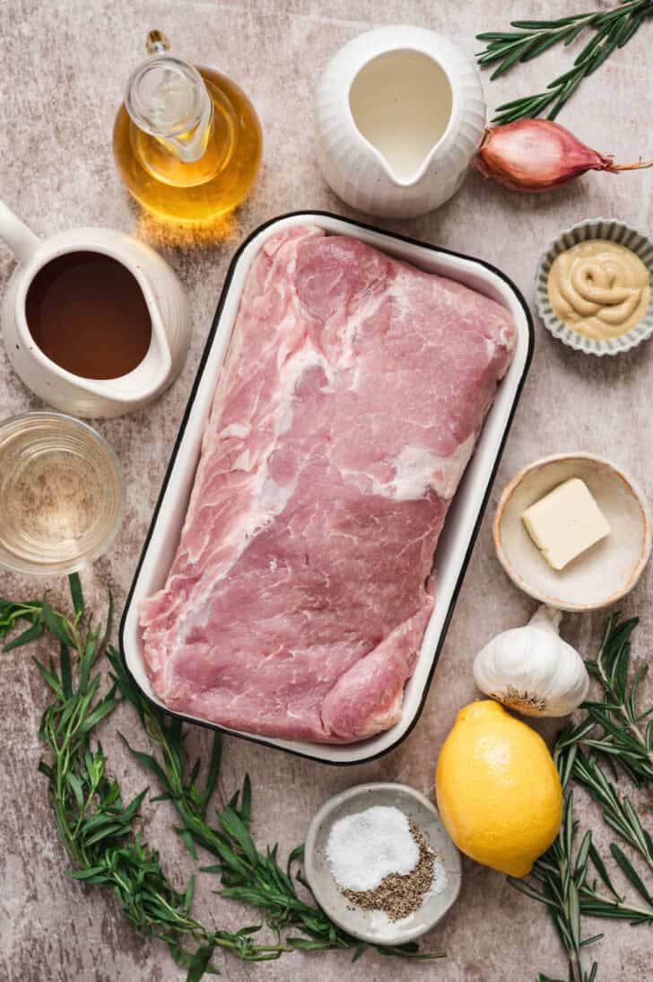 Ingredients on a light surface, including raw meat, herbs, lemon butter, shallot, garlic, oil and dairy.