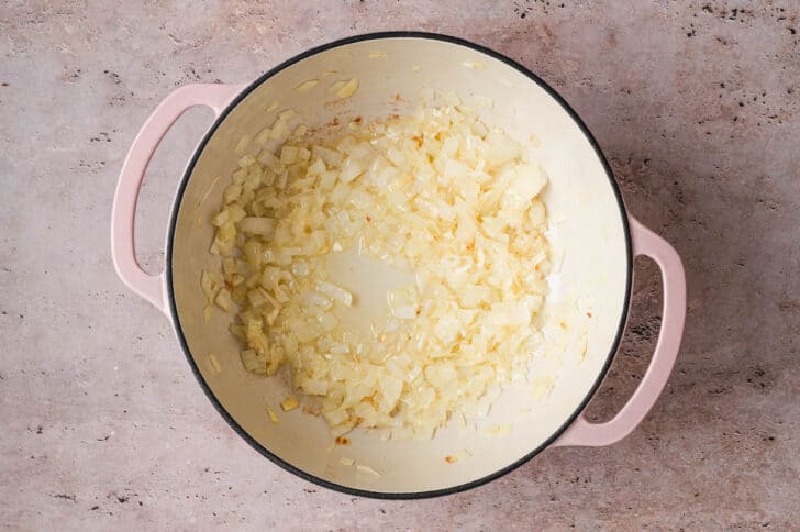 A pink Dutch oven with sauteed onions in the bottom.