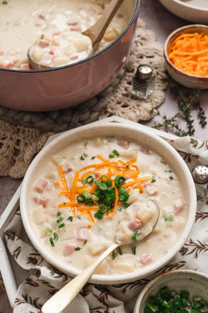 A bowl of easy ham and potato soup topped with shredded cheese and green onions.