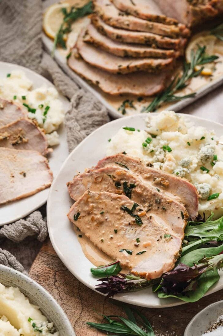 A pork loin roast recipe sliced and plated with salad and mashed potatoes.